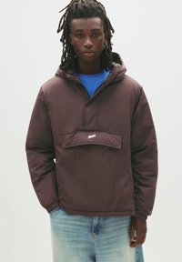 Brun, huva med pullover-jacka med en framficka och elastiska mudd; bärs över en blå skjorta; slät textur, avslappnad design, minimal varumärkesprofil.
