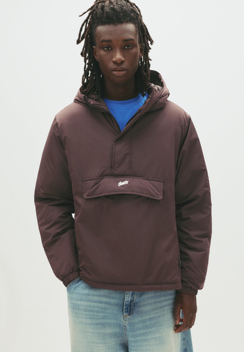 Brun, huva med pullover-jacka med en framficka och elastiska mudd; bärs över en blå skjorta; slät textur, avslappnad design, minimal varumärkesprofil.