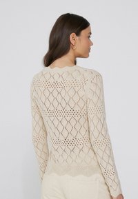 Beżowy sweter wykonany na drutach, z wzorem w diamenty, otwartą siateczką, falbaniastym dekoltem i dopasowanymi długimi rękawami.