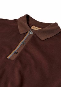 Braunes Poloshirt mit einem kontrastierenden braunen Kragen, das drei schwarze Knöpfe und blau-goldene Streifenakzente in der Nähe des Knopfleisten bietet.