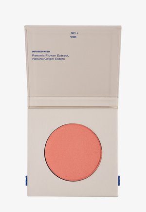 Róż w proszku w okrągłym pojemniku, miękki kolor koralowy z matowym wykończeniem; umieszczony w kwadratowym kremowym kompaktowym opakowaniu z niebieskim akcentem.