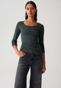 Donkergroen langemouwen shirt met een scoopnekkraag en een aansluitend design, gecombineerd met zwarte wijde jeans met een soepele textuur.