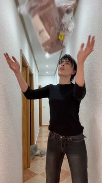 Persoon in zwart shirt vangt een in plastic verpakt voorwerp dat wordt gegooid in een smalle, fel verlichte gang met betegelde vloer.