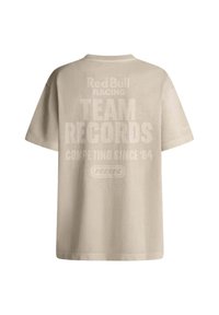 Bežové bavlnené tričko s krátkymi rukávmi. Na zadnej strane sa nachádza veľký text: "Red Bull Racing TEAM RECORDS COMPETING SINCE '04" spolu s logom.