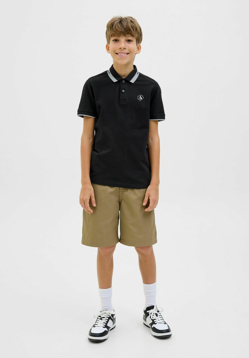 Zwart poloshirt met grijze accenten, kaki shorts, witte sokken en zwarte sneakers. Poloshirt heeft een logo en een knoopsluiting met drie knopen.
