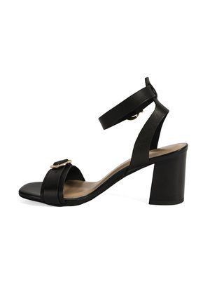 Black open-toe sandal with an ankle strap, square heel, gold-tone hardware, and flat sole. Made from smooth leather with a matte finish.