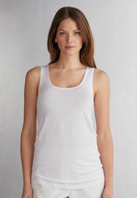 Top bianco senza maniche con scollo a barca, spalline sottili e silhouette aderente. Realizzato in tessuto morbido e liscio con una leggera lucentezza.
