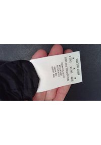 Černá nylonová látka s návěskem, na kterém je uvedeno "100% nylon", "velikost M" a "vyrobeno v Laosu". Návěs je bílý s černým textem.