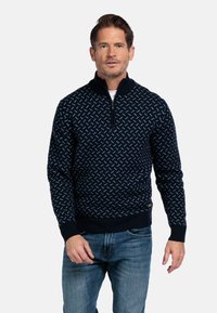 Navy zip-necksweater met een geometrisch patroon in lichtblauw. Gebreide textuur met ribgebreide manchetten en zoom, gecombineerd met blauwe jeans.