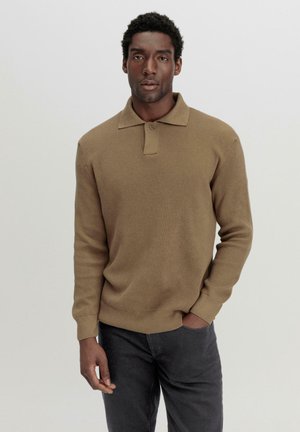 Bruine geribbelde gebreide polo met een kraag en knoopsluiting, gecombineerd met donkergrauwe broeken. De stof lijkt zacht en gestructureerd.