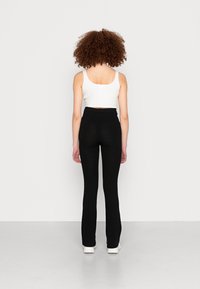 Top cropped branco com texturas, combinado com calças flare de malha preta de cintura alta e calçado branco, mostrado de costas contra um fundo simples.