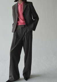 Ciemnoszary garnitur na miarę z dopasowanym żakietem i szerokimi spodniami, zestawiony z jaskrawo różową koszulą z kołnierzykiem. Gładka tkanina, elegancki design.