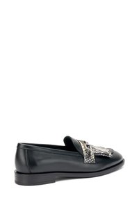 Mocassino in pelle nera con suola piatta, caratterizzato da un accentuato decorativo metallico e con motivo sulla punta. Texture liscia, design classico.
