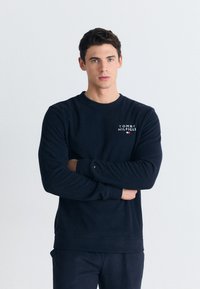 Námořnická modrá mikina vyrobená z bavlněné směsi, má kulatý výstřih, dlouhé rukávy a logo "TOMMY HILFIGER" na hrudi.