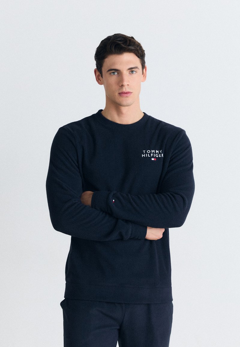 Námořnická modrá mikina vyrobená z bavlněné směsi, má kulatý výstřih, dlouhé rukávy a logo "TOMMY HILFIGER" na hrudi.