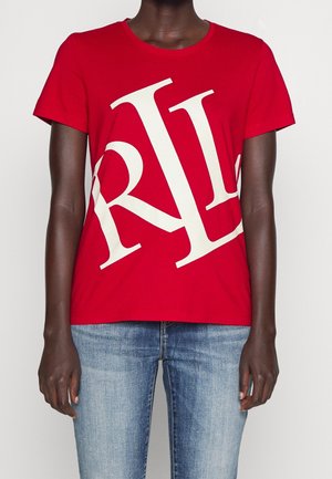 Person trägt ein rotes Kurzarmshirt mit großen weißen Buchstaben "RL" diagonal über der Vorderseite und blaue ausgewaschene Jeans.