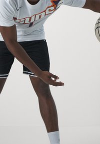 Vit atletisk t-shirt med "Suns"-logga i orange och marinblå, tillsammans med svarta shorts med vita sidostripes; basketboll i handen.