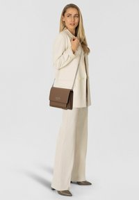 Bolso cruzado de cuero marrón con solapa y logo dorado. Presenta una correa de cadena plateada, forma rectangular, textura suave y diseño minimalista.