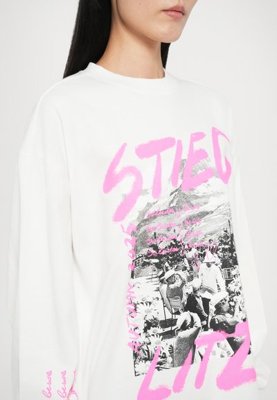 White long-sleeve t-shirt featuring a graphic print with a black-and-white image and pink text, creating a bold contrast and modern design.