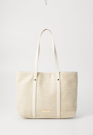 Sac cabas beige tissé avec des anses en cuir crème et une petite étiquette de marque rectangulaire à l'avant, présenté sur un fond blanc.