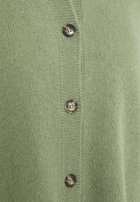 Zelený pletený cardigan s rytou texturou a pěti knoflíkovými zapínáními. Knoflíky jsou tmavé s mramorovým povrchem a čtyřmi otvory.