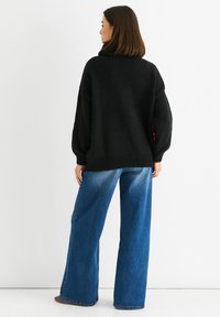 Černý oversized svetr s texturovaným povrchem, s vysokým límcem a spadlými rameny, doplněný o široké modré džíny.