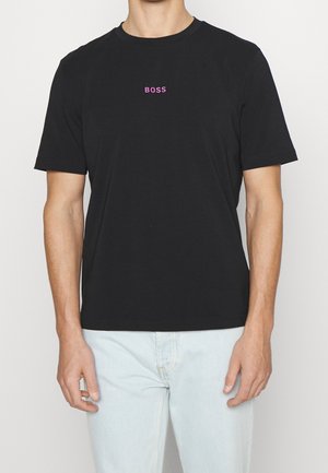 Person trägt ein schwarzes T-Shirt mit kurzen Ärmeln und dem Wort „BOSS“ in kleinen rosa Buchstaben mittig auf der Brust.
