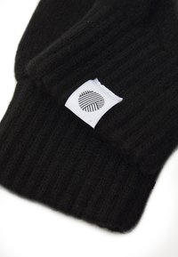 Mânuși din tricot cu nervuri negre, având o etichetă albă cu un model circular negru. Țesătura pare moale și texturată.