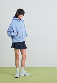 Svijetloplavi oversized dukserica s prednjim džepom, uparen s crnom suknjom i bijelim čarapama, upotpunjeno debelim bijelim tenisicama.