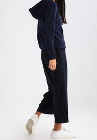Sudadera azul marino con un bolsillo frontal, puños y dobladillo acanalados. Combinada con pantalones negros fluidos y zapatillas blancas, creando un look relajado.
