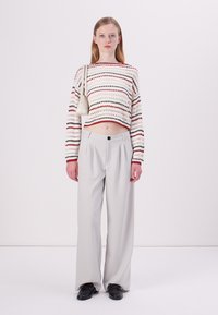 Striped knit crop sweater in cream, red, and black; wide, gray trousers with a front button; black shoes; shoulder bag in light color.