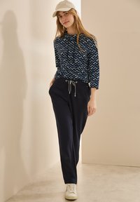 Navy-tyylinen huppari, jossa on huppu, paritettu navy-housujen kanssa, joissa on säädettävä nauha. Täydennetty valkoisilla lenkkareilla.
