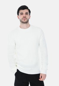 Maglione bianco a maglia con motivo testurizzato, scollatura rotonda e maniche lunghe, abbinato a pantaloni cargo neri.