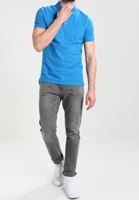 Polo bleu à manches courtes avec patte de boutonnage à deux boutons ; jean gris ; baskets blanches. Texture lisse, coupe décontractée, style casual.