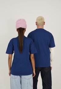 Mørkeblå bomulds t-shirts på to personer, hvor den ene har en fluffy lyserød hue på. Den anden persons t-shirt har en lys langærmet skjorte under.