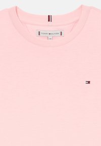 Lys lyserød bomulds T-shirt med rund hals, korte ærmer og et lille broderet logo i rød, hvid og blå på brystet.