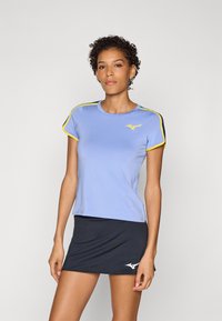 Camiseta atlética de manga corta en azul claro con detalles amarillos en el cuello y las mangas, combinada con una falda negra con un logo.