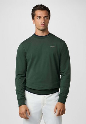 Sweatshirt vert foncé à col rond, avec des poignets et un ourlet côtelés. Présente un petit logo brodé sur la poitrine et un détail de col superposé.