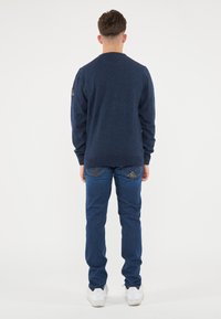 Maglione a maniche lunghe blu navy realizzato in tessuto testurizzato, abbinato a jeans blu con cuciture dettagliate e sneakers bianche.