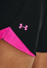 Pantalones cortos deportivos negros con un acento rosa en el dobladillo. Presenta un logo de Under Armour en rosa en el lado inferior. Textura suave, diseñado para la comodidad.