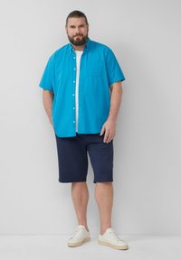 Turquoise overhemd met korte mouwen en knopen, marineblauwe shorts, crèmekleurige sneakers. Heeft een borstzakje en een losse pasvorm. Eenvoudig ontwerp, casual stijl.