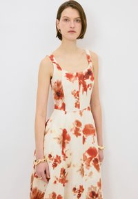 Vestido floral en crema con grandes estampados de flores rojas y naranjas, corsé ligeramente ajustado, escote cuadrado y falda acampanada.