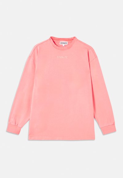 Langermet skjorte i korallrød rosa, laget av mykt stoff. Har en rund halslinning og elastiske mansjetter med "STIEGLITZ" trykt på brystet.