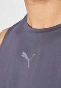 Ærmeløs atletisk top i mørkegrå stof, med en glat tekstur og et lysepurpur Puma-logo ved brystområdet.