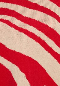 Rood en beige gestreepte gebreide stof met opvallende golvende lijnen. De textuur is zacht, met een fijne brei en een licht glanzende afwerking.