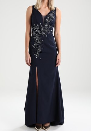 Granatowa wieczorowa sukienka bez rękawów z kwiatowymi zdobieniami z koralików i rozcięciem z przodu, noszona z metalicznymi butami na obcasie z ostro zakończonym noskiem.