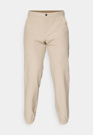 Beige pants made of smooth fabric, featuring an elastic waistband, two side pockets, and elastic cuffs at the ankles.