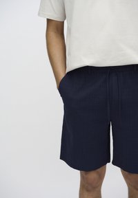 Shorts bleu marine en tissu texturé, munis d'une taille élastique avec cordon de serrage et de poches latérales, associés à un t-shirt blanc.