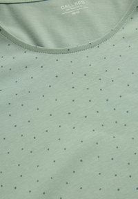 Ljusgrön T-shirt med rund halsringning, tillverkad av mjukt tyg, med små mörkblå prickar jämnt fördelade över ytan.