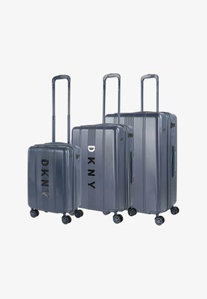 Tres maletas rígidas en gris con estrías verticales, que presentan la marca "DKNY" en negro, asas extensibles y ruedas giratorias.